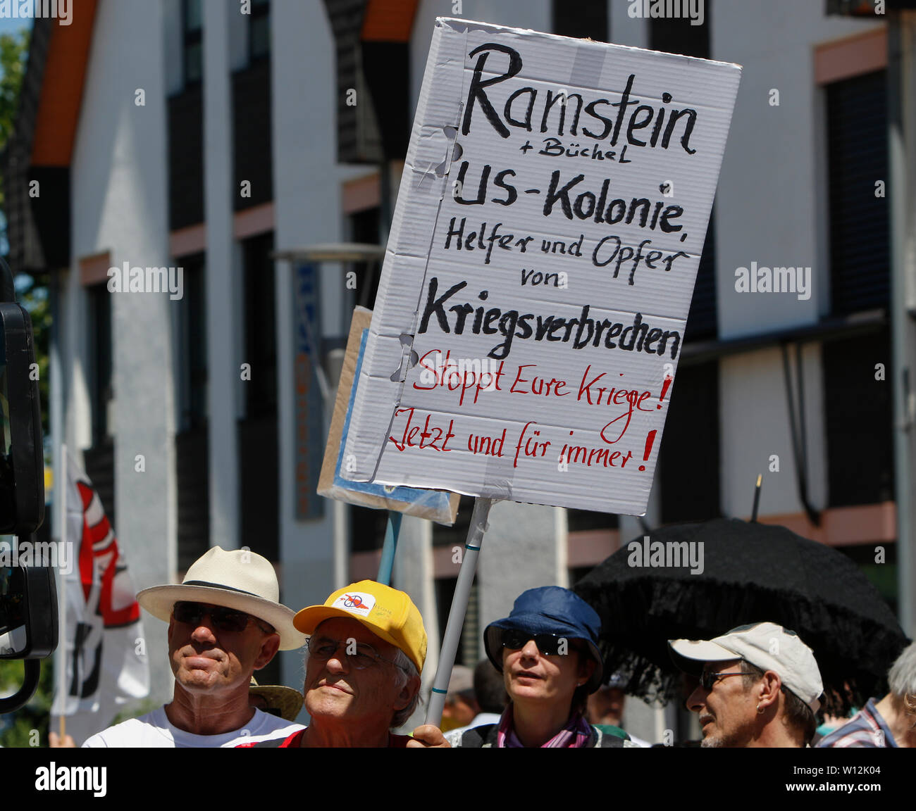Ramstein, Germany. 29th June 2019. A protester holds up a sign that reads 'Ramstein `Buchel - US colony - assistants and victims of war crimes - Stop your wars! Now and forever!'.A few thousand peace activists from the Stopp Air Base Ramstein campaign protested outside the US airbase in Ramstein. The protest was the end of this year’s week of action against the airbase. The main focus of this year’s events was on the alleged involvement of the airbase in the drone warfare of the US Air Force in the Middle East and Africa and call to not use Ramstein for a future war with Iran. Stock Photo